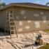 Stucco exterior of a Southwest Florida CBS home prepped for repainting with patched areas, ladder and paint sprayer