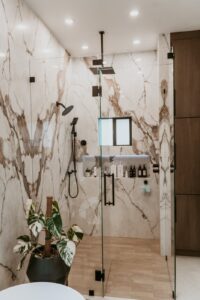 Frameless glass walk-in shower with marble walls, rainfall and handheld shower heads, and a niche shelf