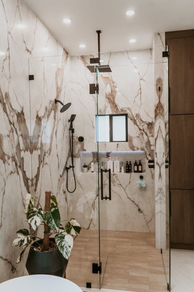 Frameless glass walk-in shower with marble walls, rainfall and handheld shower heads, and a niche shelf
