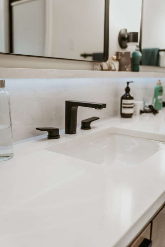 Bathroom sink with a black faucet, light backsplash, and framed mirror