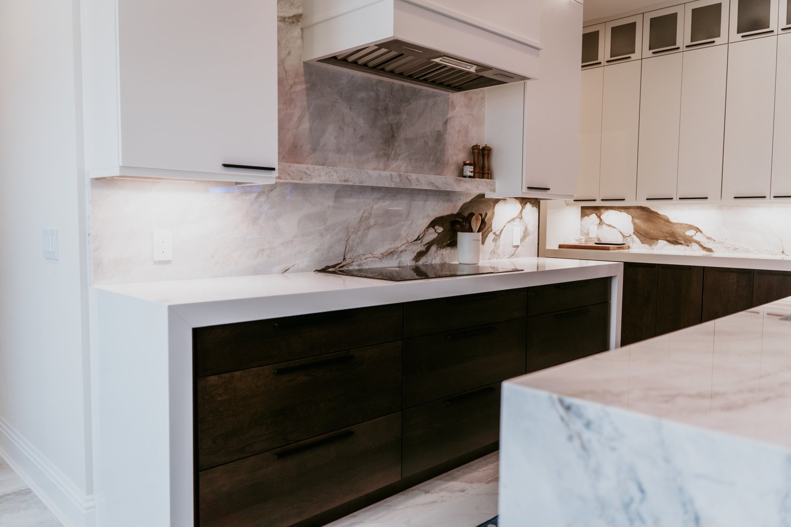 Dark cooktop and stainless hood with a full-height veined stone backsplash in a remodeled kitchen