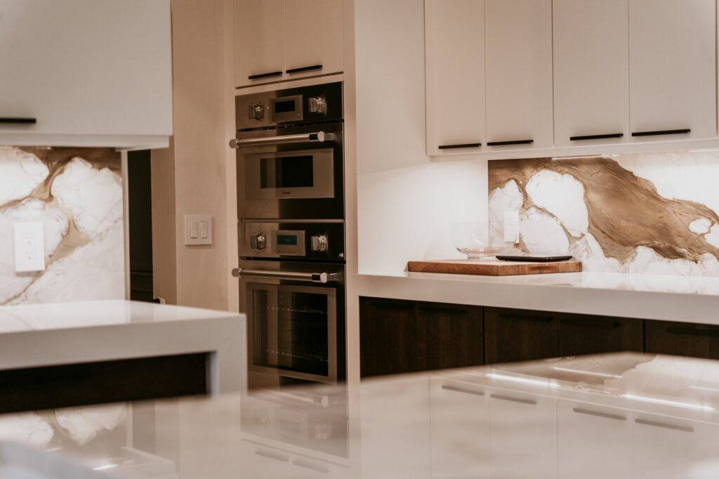 Double wall ovens beside white cabinets and a gold-veined stone backsplash