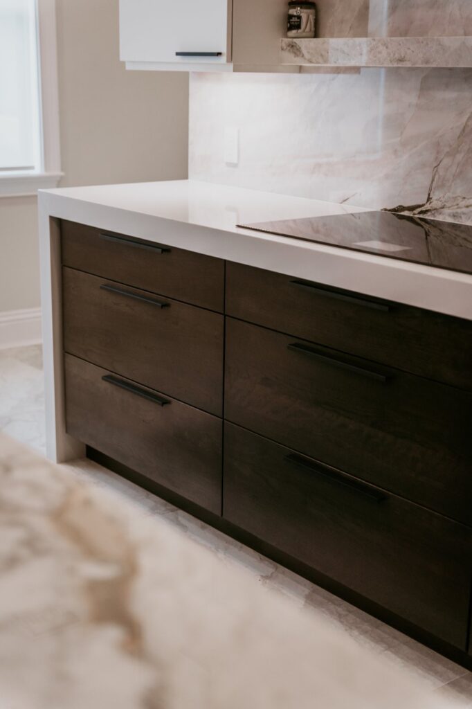 Close-up espresso wood drawers with black pulls under quartz counter and cooktop.