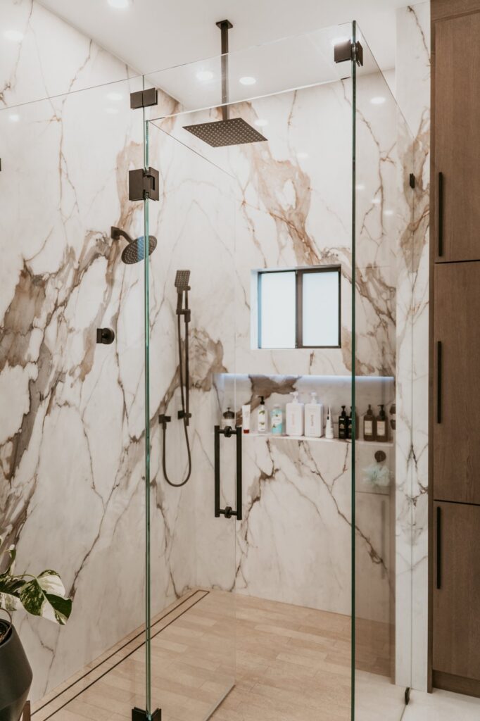 Large frameless glass shower, calacatta surround, black rain + handheld, lit niche.