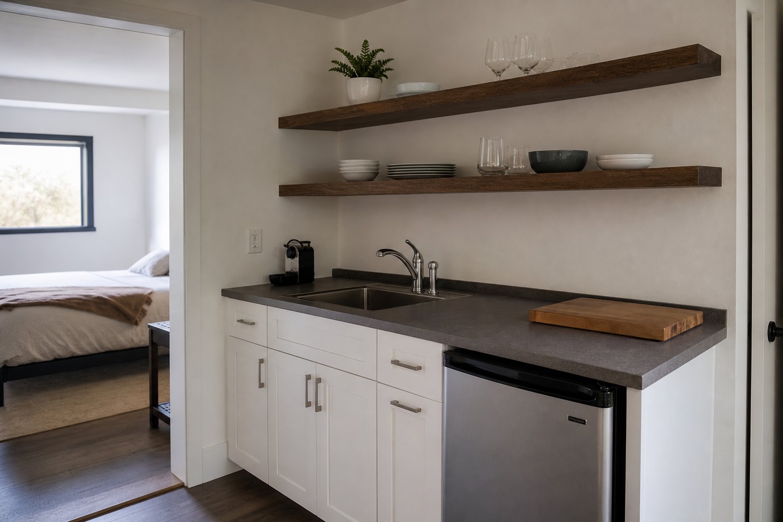 Compact kitchenette with white cabinets, small sink, and open shelving in a converted guest suite