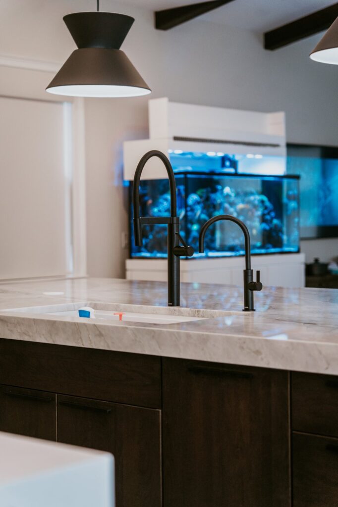 Marble island sink and black faucet against a large reef aquarium.