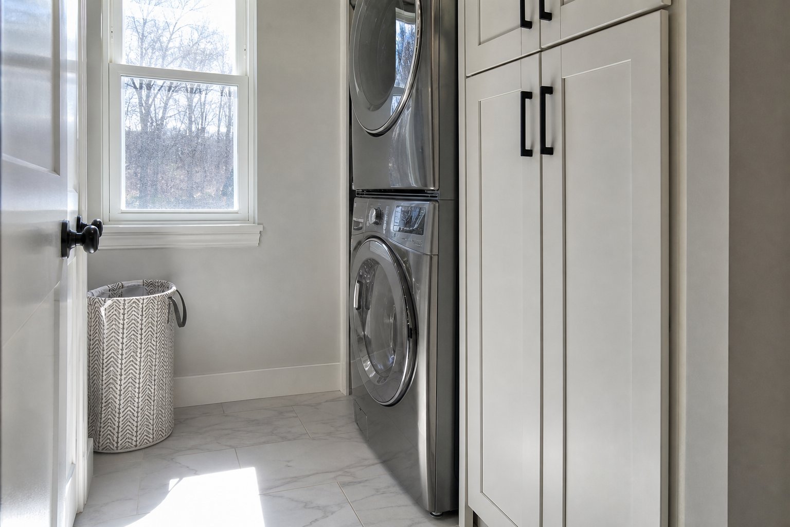 Tall storage cabinet beside stacked washer and dryer on porcelain tile flooring