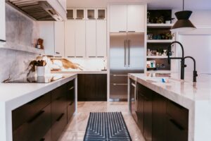 Wide kitchen: dark cabinets, white waterfall island, marble backsplash, fridge, black faucet.