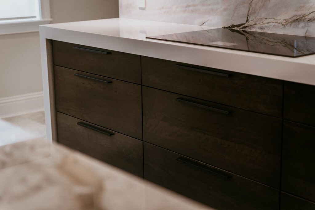 Close-up of dark wood base drawers with black bar pulls and white waterfall countertop edge.