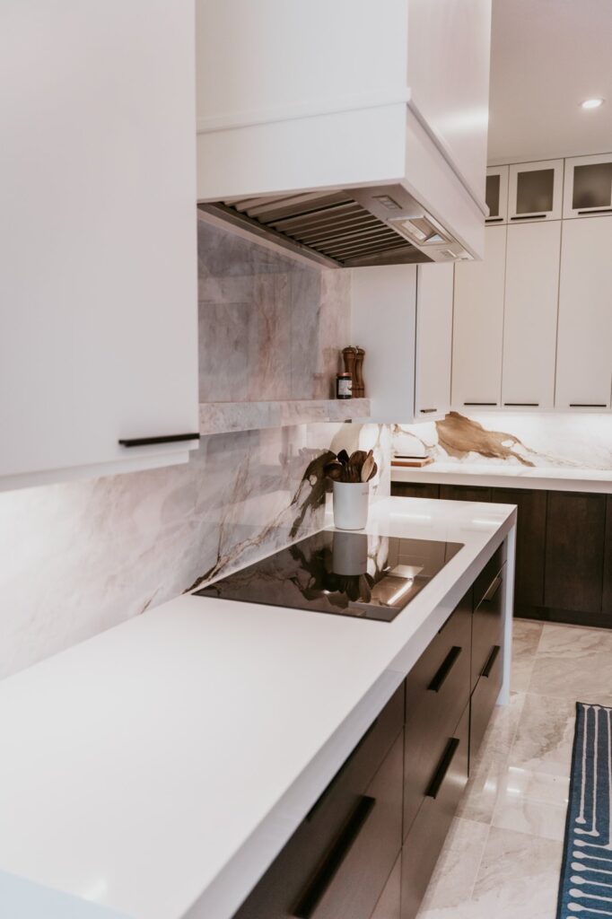Induction cooktop on white waterfall counter under stainless hood with marble backsplash.