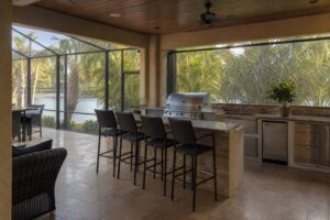 Full outdoor kitchen with built-in grill, bar seating, and stone counters on a covered SWFL lanai