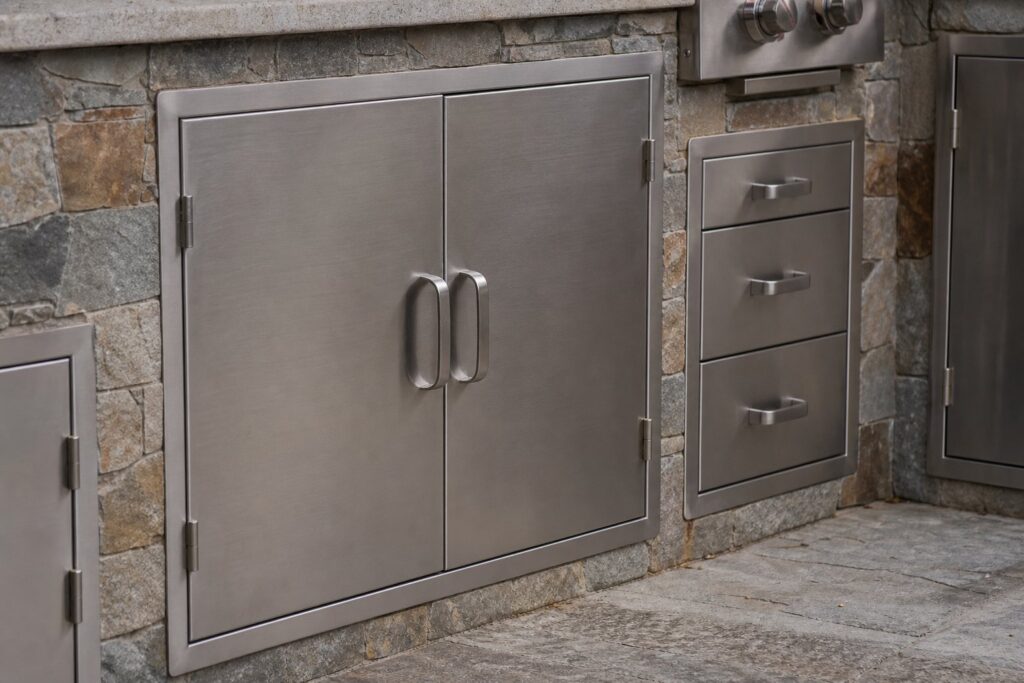 Brushed stainless access doors and drawers in a stone-clad outdoor kitchen