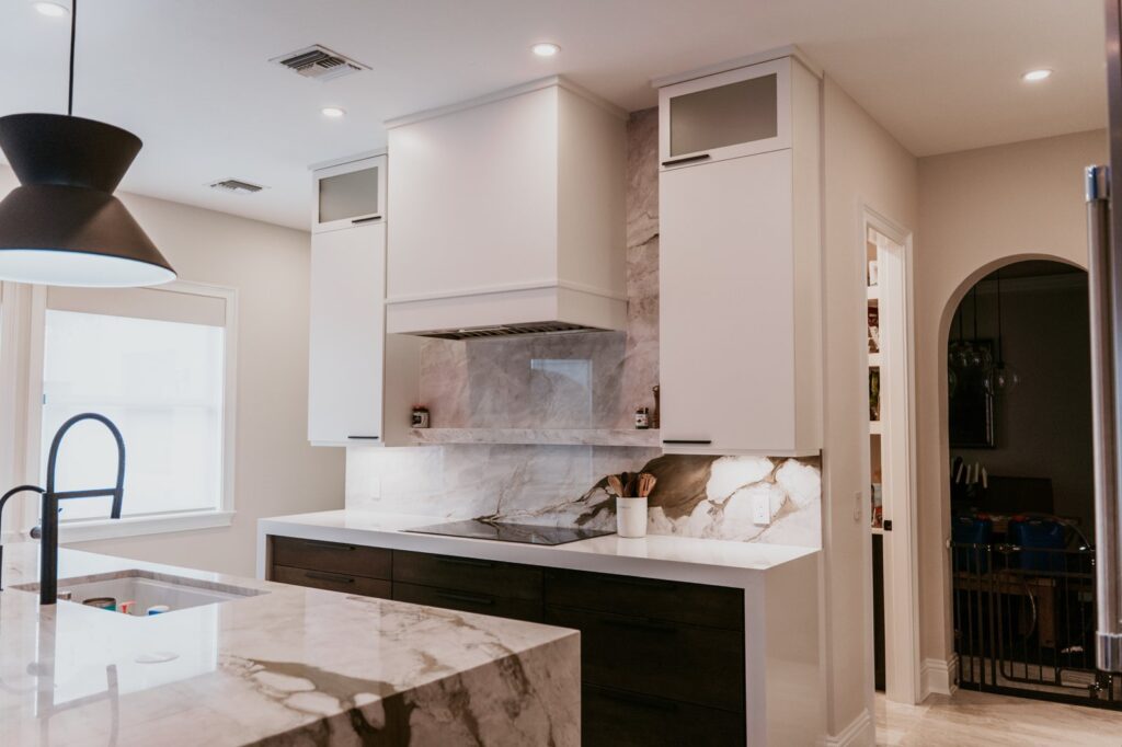 Wide kitchen: hood/cooktop range wall, calacatta waterfall island, arched pantry doorway.