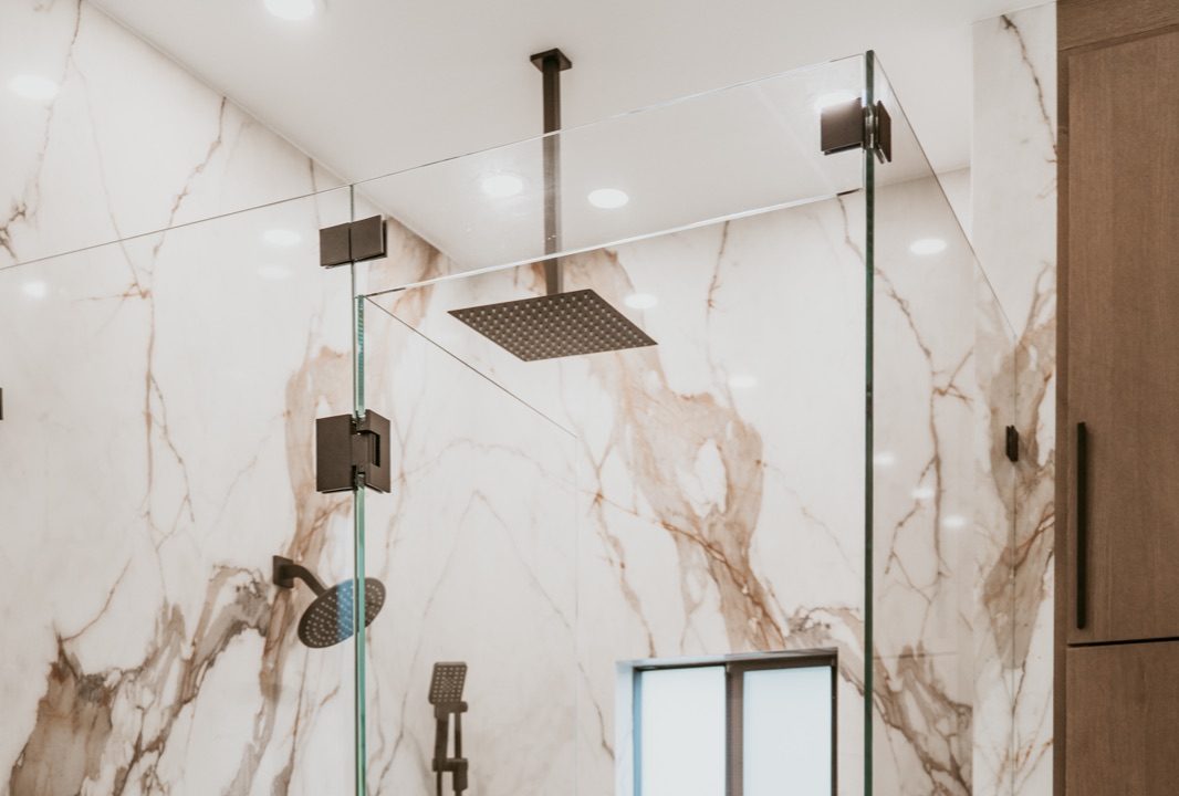 Large-format marble-look tile aligned around frameless glass and a rain shower