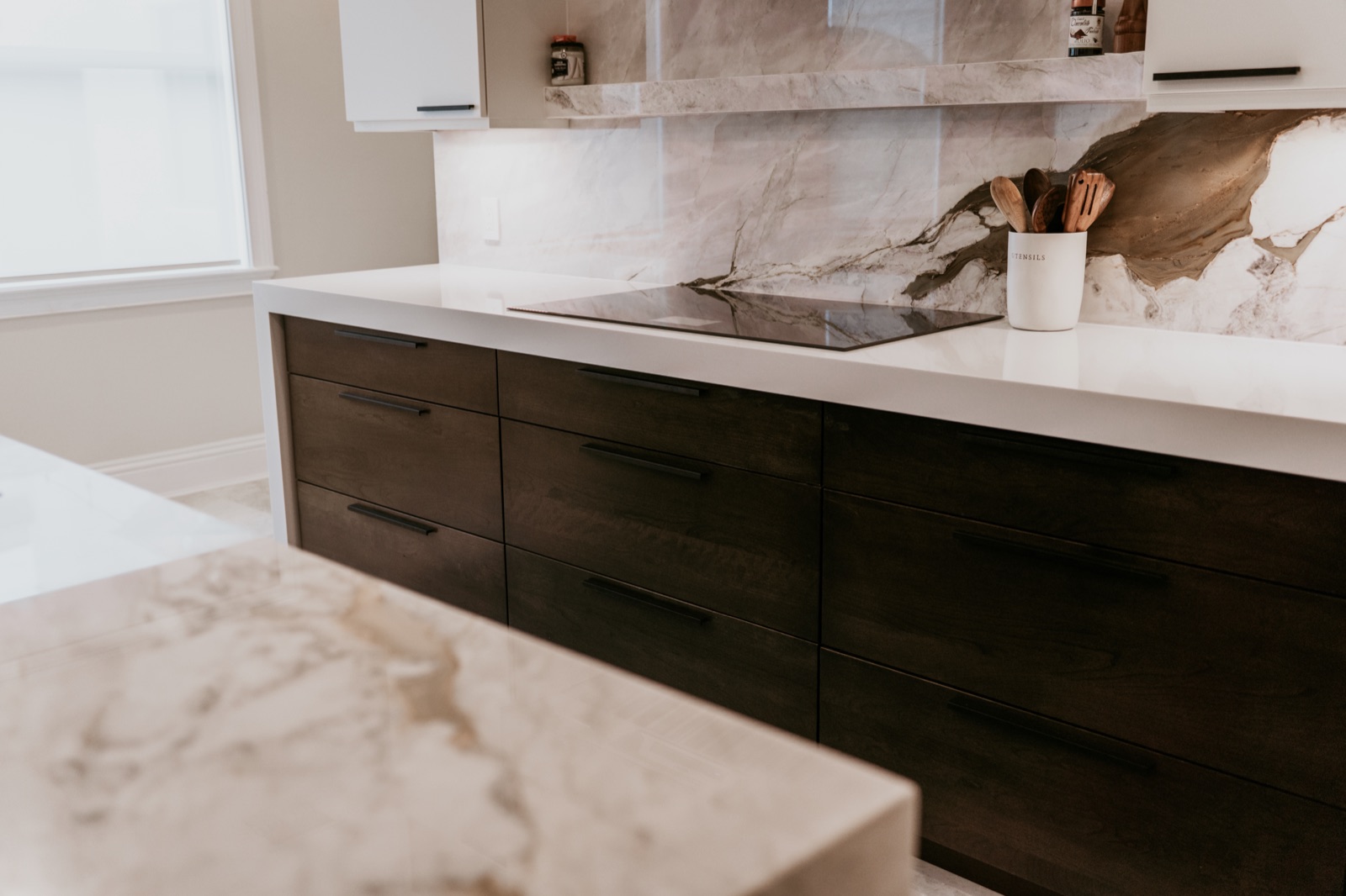 Light stone countertop edge above dark drawer fronts and matte-black pulls