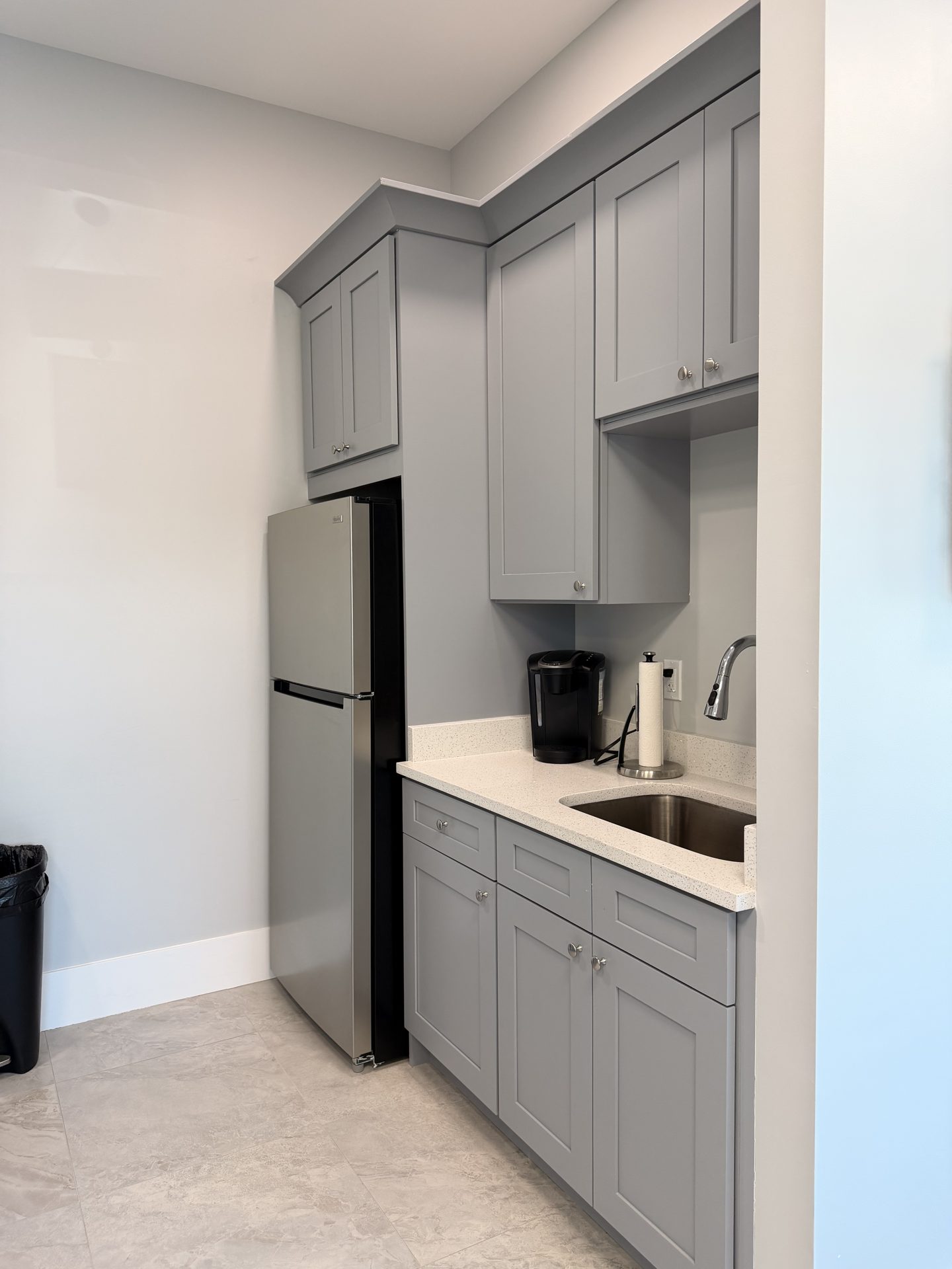 Gray kitchenette cabinets with compact stainless refrigerator, undermount sink and coffee station