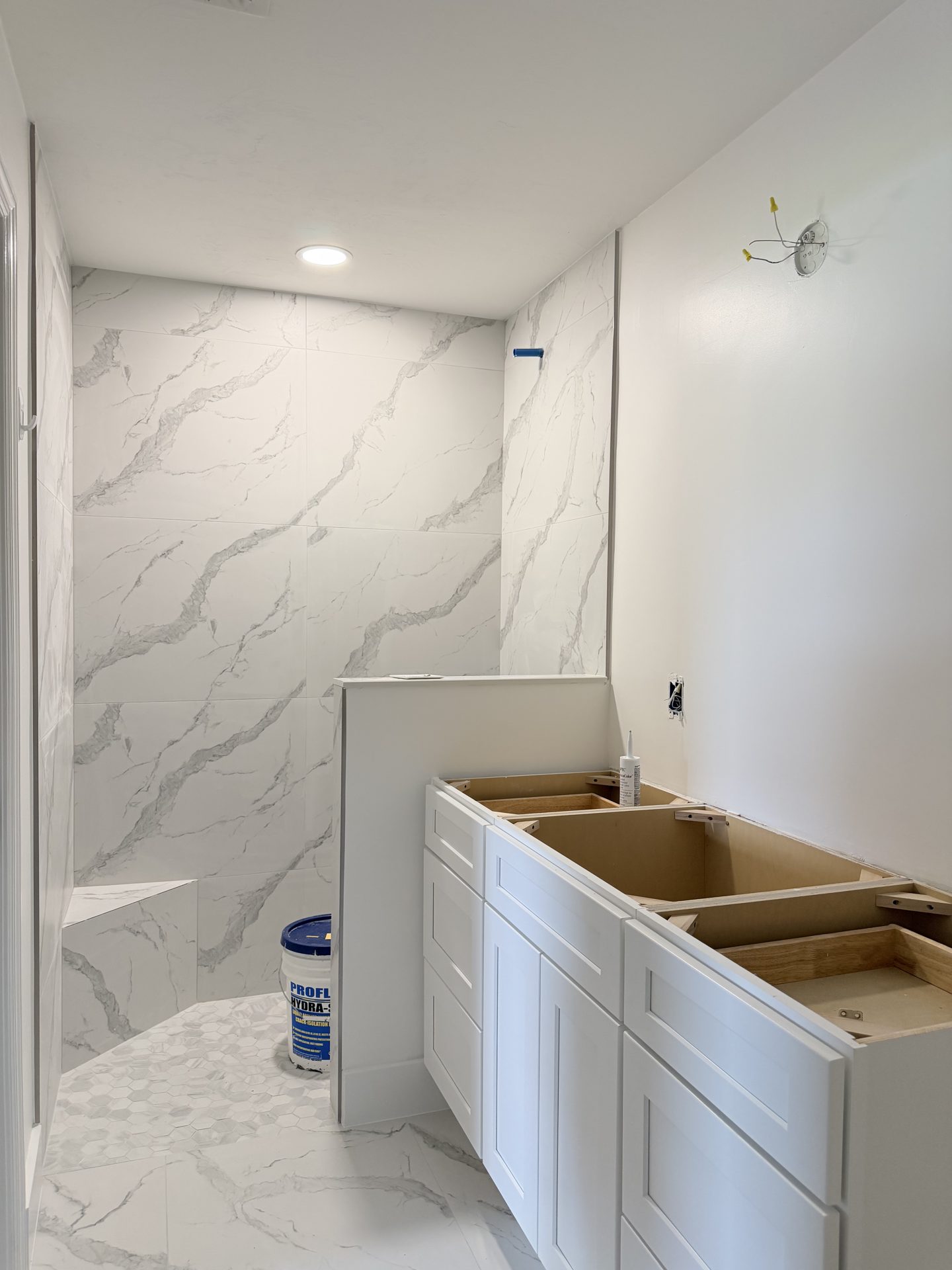 Master bathroom during remodel with marble look slab shower walls and white vanity cabinets being installed