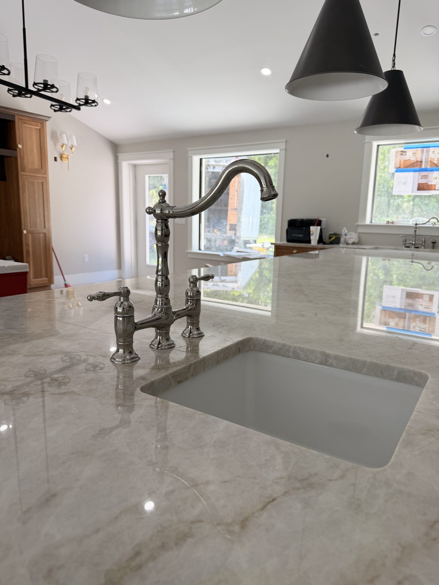 Polished nickel bridge faucet over an undermount sink in a veined stone countertop