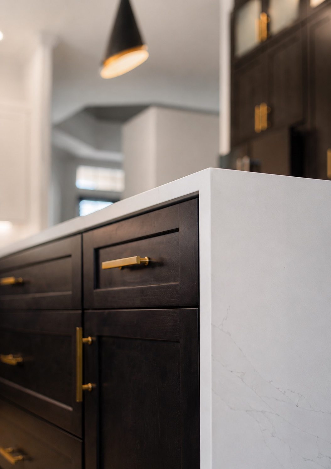 Espresso shaker island cabinets with brass hardware under a white quartz waterfall countertop
