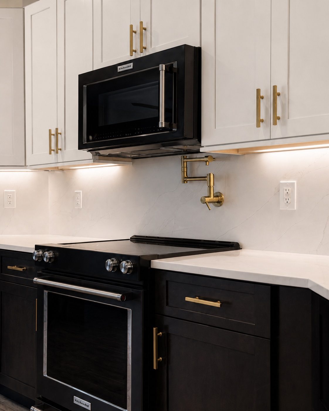 KitchenAid black stainless microwave and range with white shaker uppers and brass pulls