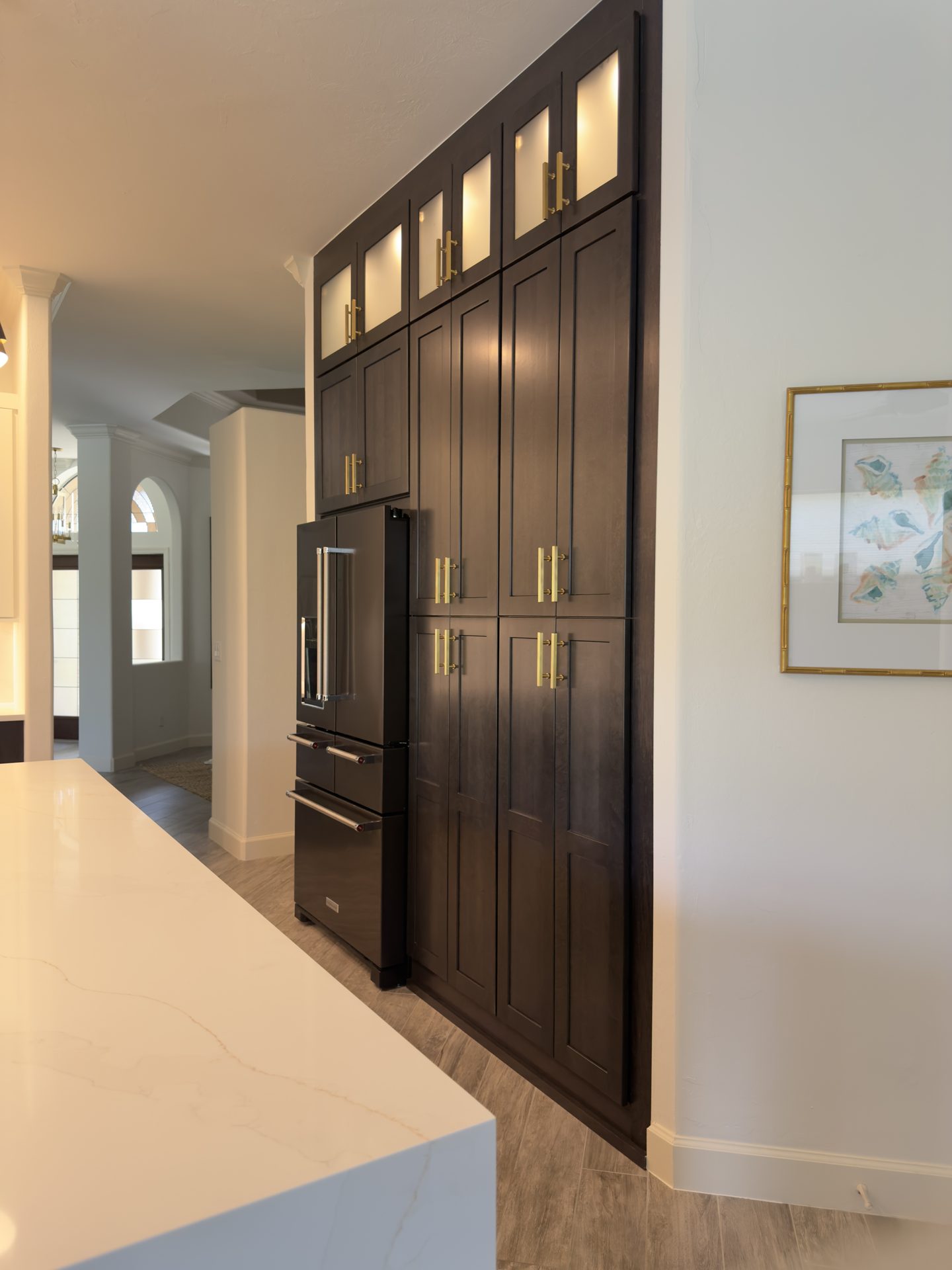 Espresso pantry wall with lighted glass front upper cabinets and brass pulls