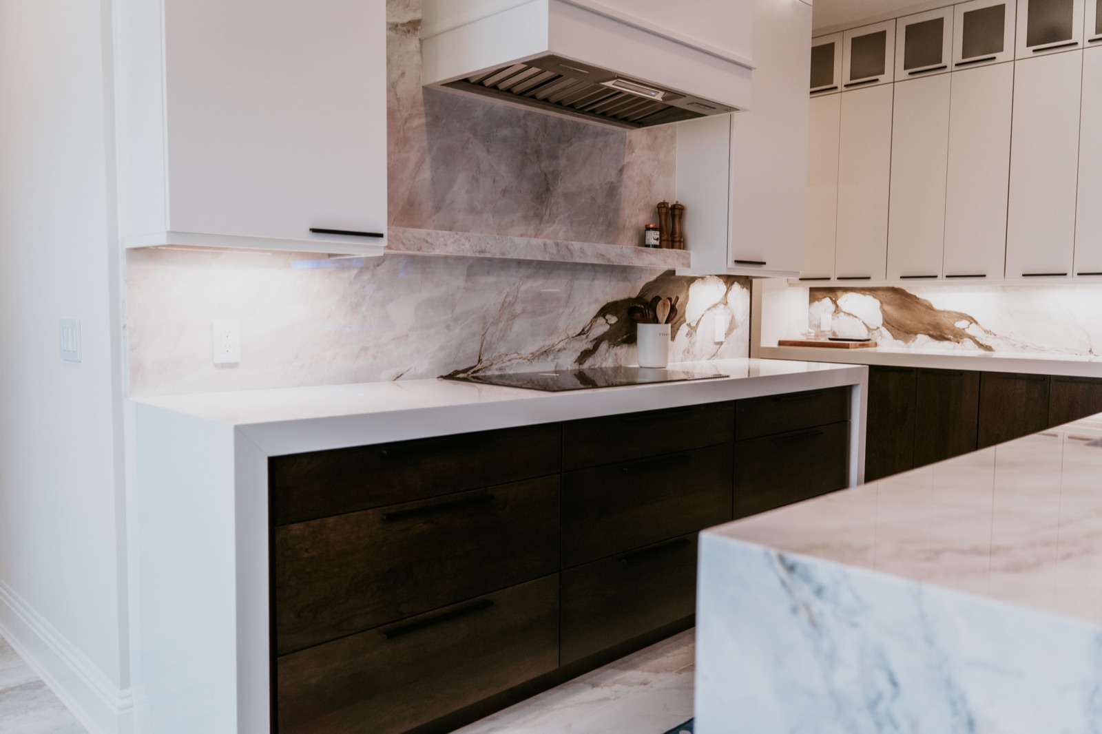 Range-wall cabinetry with a marble backsplash and integrated task lighting