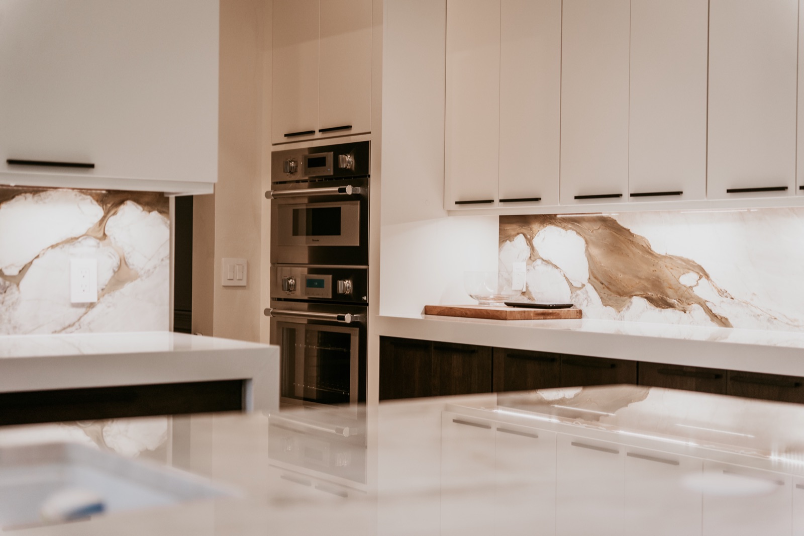 Wall-oven cabinetry beside an illuminated marble backsplash