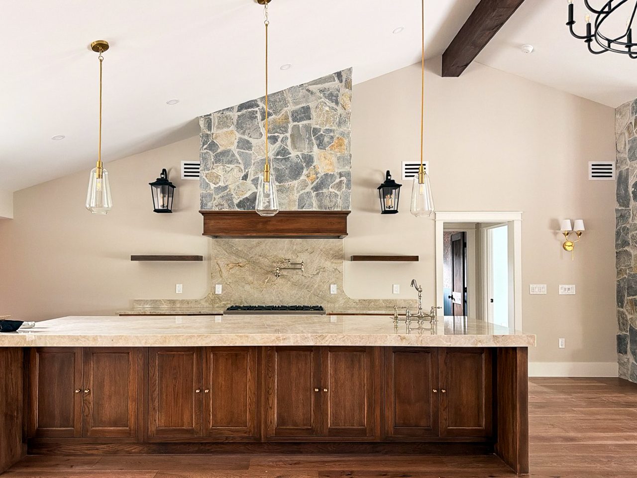 Finished stained oak kitchen island with Taj Mahal quartzite top, glass pendants and a stacked stone range hood wall in a Fort Myers whole home remodel