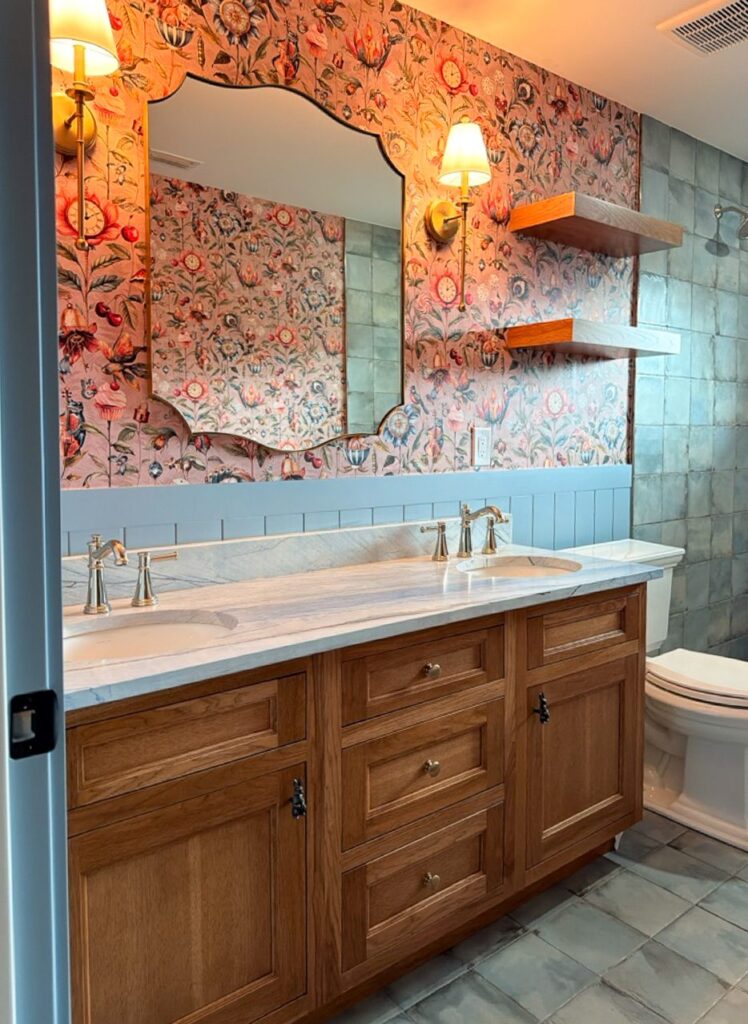 Guest bath with a stained wood double vanity, blue quartzite counter, blue V-groove wainscot, floral wallpaper and scalloped mirror