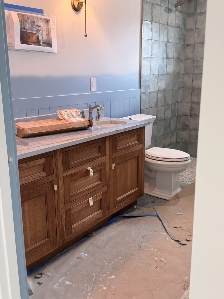 Guest bath during the final stage with the stained wood vanity and shower tile set and floor protection down