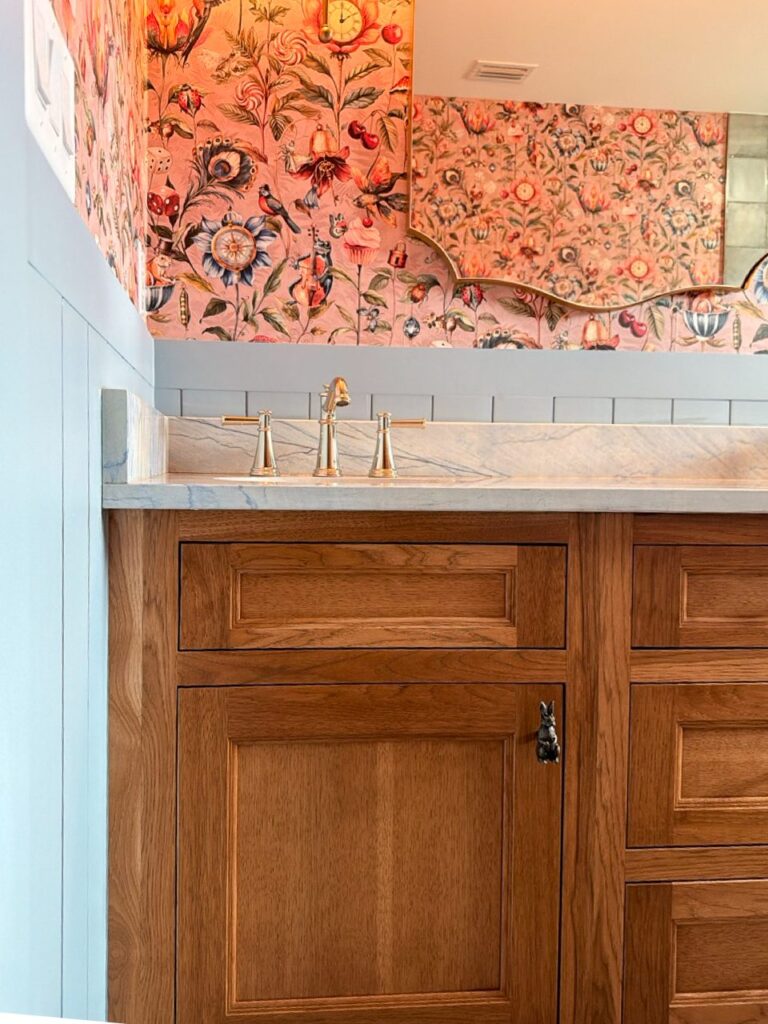 Stained wood guest bath vanity with a blue V-groove wainscot, tile strip and floral wallpaper above