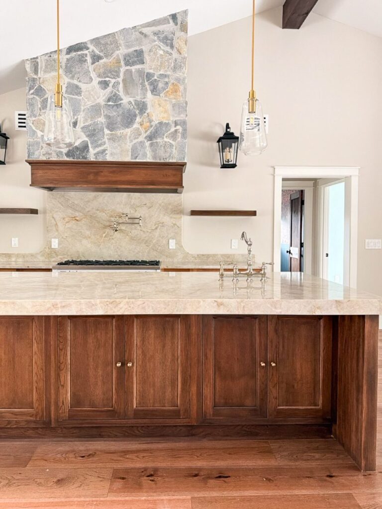 Finished stained oak island with Taj Mahal quartzite top facing a stacked stone hood wall with lantern sconces