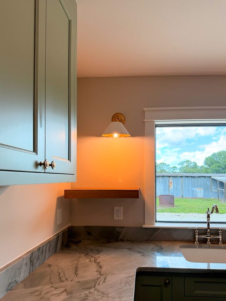 Laundry room window wall with a brass sconce, floating wood shelf and veined stone counter