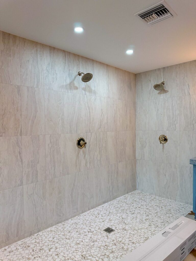 Large walk-in shower with two shower heads, large format wall tile and a pebble mosaic floor