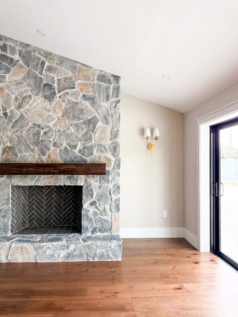 Floor to ceiling stacked stone fireplace with a herringbone firebox and wood beam mantel on wide plank floors