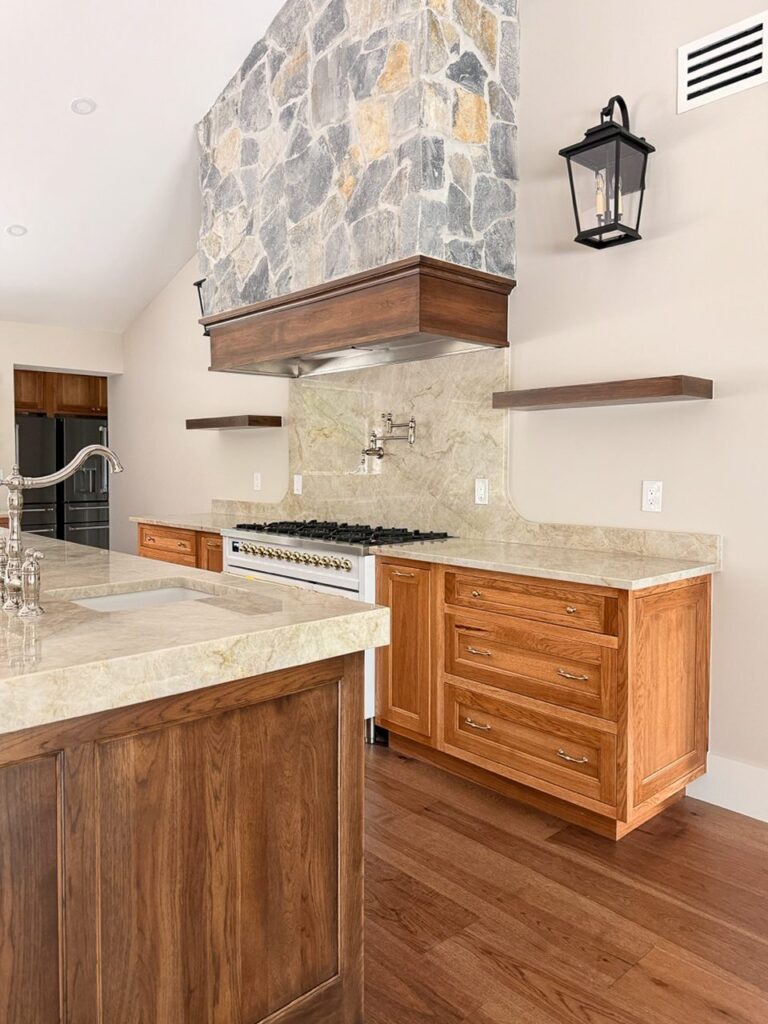 Stacked stone chimney over a wood clad range hood with a slab backsplash and floating shelf in a remodeled Fort Myers kitchen