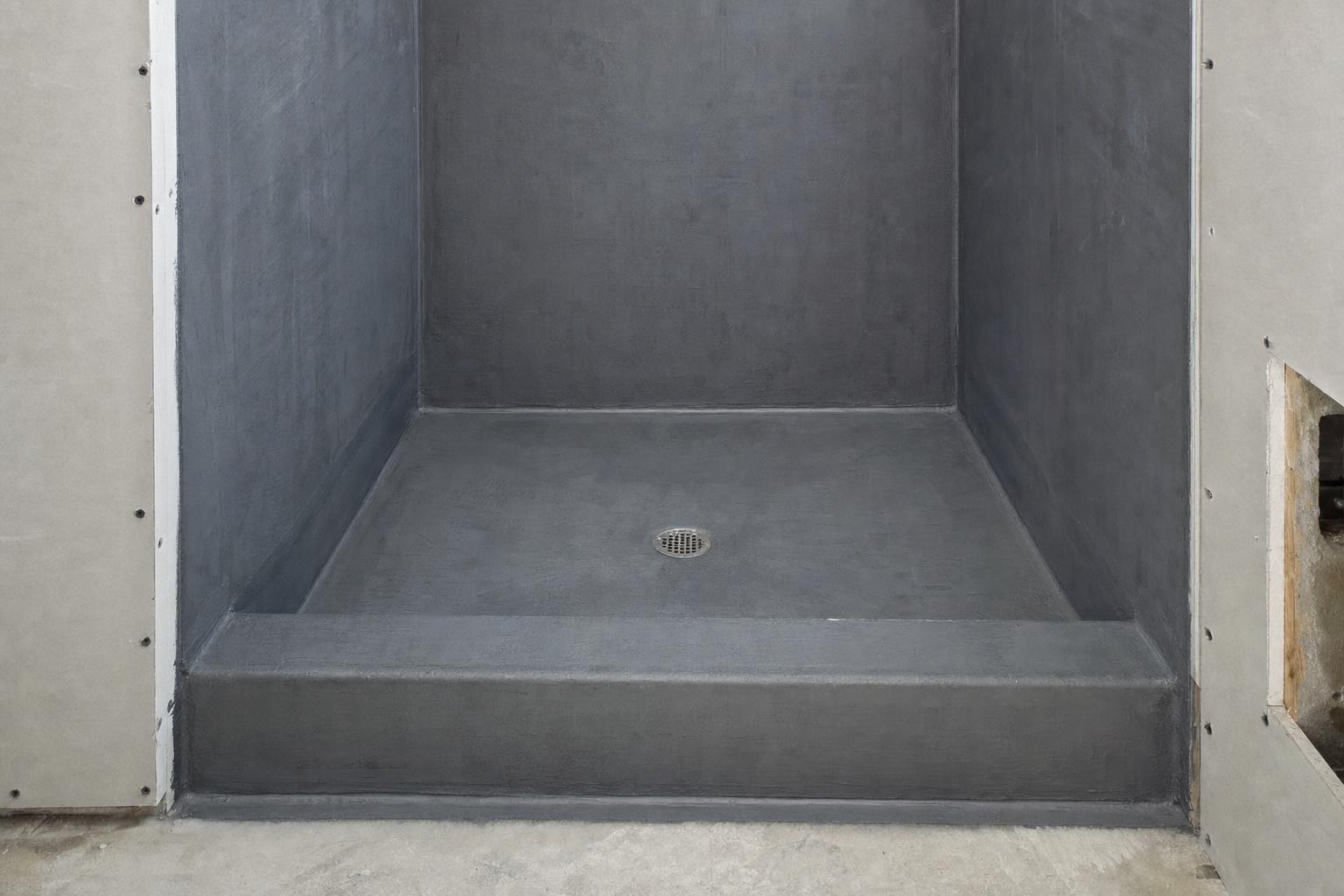 Shower stall coated in waterproofing membrane with a sloped floor, round drain, and curb