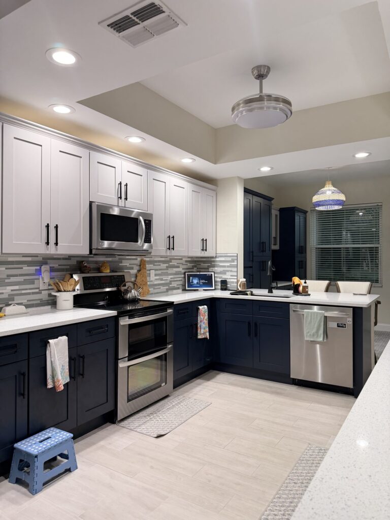 Wide view of the finished kitchen with light gray uppers, navy lowers, white counters and a window wall