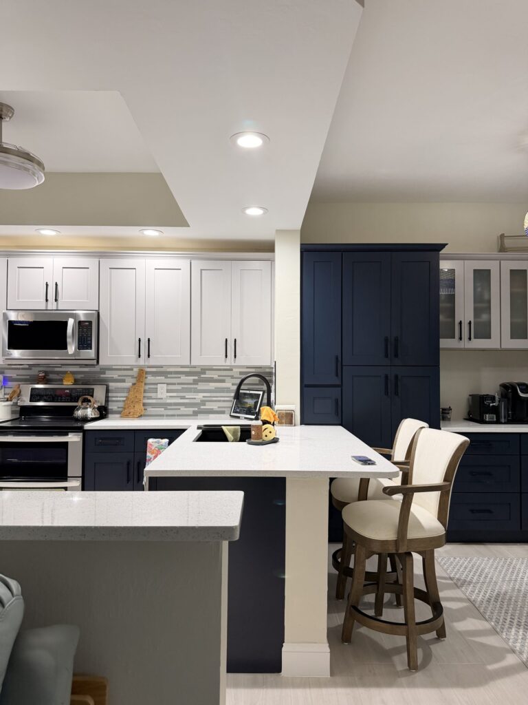 Kitchen island with counter stools seen from the living area, with navy pantry towers and light gray uppers behind