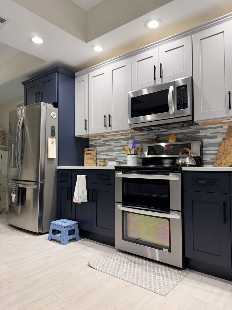 Kitchen range wall with light gray shaker upper cabinets over navy shaker lower cabinets and a navy tall cabinet